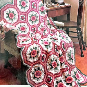 May include: A crocheted blanket with a pink, white, and green floral pattern. The blanket is draped over a chair.