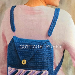 Może przedstawiać: Niebieski plecak wykonany na szydełku z kieszenią w paski i zapięciem na guzik. Na plecaku widoczny jest napis "COTTAGE PUPPY".