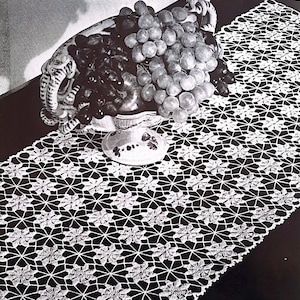 Könnte beinhalten: Ein weißer gehäkelter Tischläufer mit einem zarten Blumenmuster. Eine Schale mit Trauben steht auf dem Läufer.