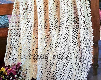 May include: A white crocheted blanket with a delicate lace pattern. The blanket is draped over a wooden bed frame and has a scalloped edge.
