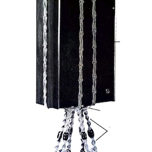 May include: Macrame plant hanger with a black rectangular object suspended from the top. The hanger is made of light-colored rope with dark beads. A white pot with a plant is at the bottom. The text "Color photo on page 6" is visible.