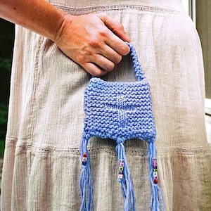 Könnte beinhalten: Eine kleine blaue Stricktasche mit Fransen und bunten Perlen. Die Tasche hat ein schlichtes Design und ist perfekt für kleine Gegenstände.