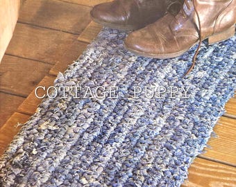May include: A blue denim doormat crocheted from strips of old jeans. The doormat is on a wooden floor and has the text "COTTAGE PUPPY" printed on it.