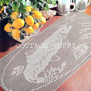 Op de afbeelding: Een witte gehaakte tafelloper met een delicaat bloemenpatroon. De loper ligt op een bruine tafel met twee mokken en een kom met citroenen.