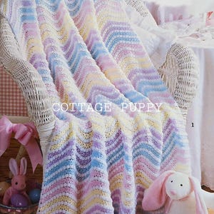 May include: A pastel colored crochet baby blanket with a chevron pattern. The blanket is draped over a white wicker chair. The blanket is made with a soft yarn and has a delicate texture.