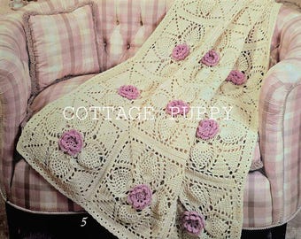 May include: A crocheted throw blanket with a square pattern and pink flower accents. The blanket is draped over a pink and white plaid couch.