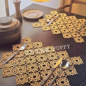 May include: Two crocheted placemats with a delicate, intricate pattern in a light beige color. The placemats are on a dark brown wooden table with silverware on top.