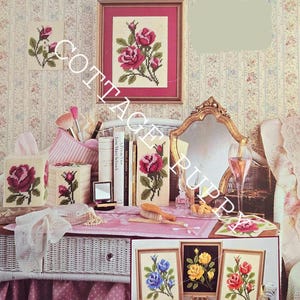 May include: A set of framed needlepoint designs featuring floral motifs. The designs include red roses, blue flowers, yellow flowers, and a single red rose. The frames are in various colours, including gold, black, and white.