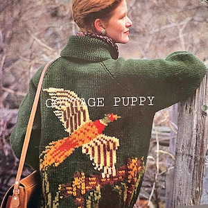 May include: A green knitted jumper with a brown pheasant embroidered on the back. The jumper has a high neck and a brown leather strap.