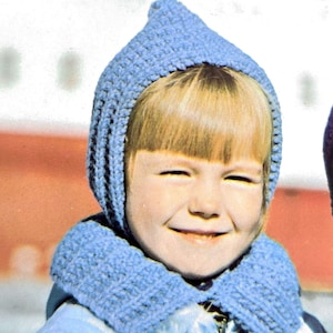 May include: A child wearing a blue knitted hat with a pointed top and a matching scarf. The hat has a long flap that can be pulled down to cover the ears.