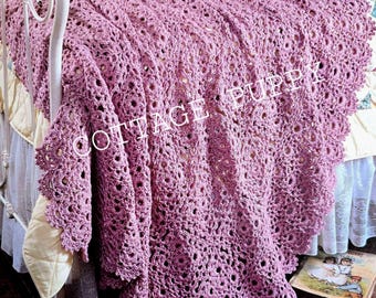 May include: A crocheted throw blanket in a light purple color with a delicate floral pattern. The blanket is draped over a white bed frame with a white and floral patterned bedspread.