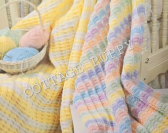 May include: Two crocheted baby blankets, one in yellow and white stripes and the other in pastel rainbow stripes, are displayed on a white cot. The blankets are made with a textured stitch. The blankets are surrounded by soft toys and yarn.
