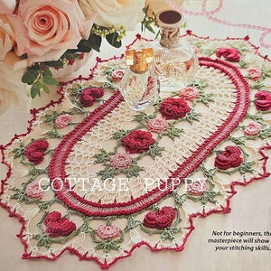May include: A white and red crochet doily with a scalloped edge and floral designs. The doily is on a white surface with a bouquet of pink roses in the background.