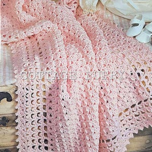 May include: A pink crocheted baby blanket with a delicate lace border. The blanket is made with a textured stitch and has a soft, feminine look.