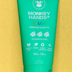 May include: A turquoise tube of hand cream with the words "MONKEY HANDS GLUEY" printed on the front. The tube is labeled "PREMIUM QUALITY" and has a sticker with a monkey graphic. The tube is 50 ml or 1.6 oz.