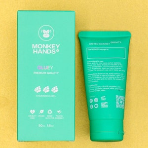 Pu&ograve; includere: Un tubo verde di crema per le mani con le parole "United Against Gravity" e "This Monkey belongs to..." sul davanti. Il retro del tubo elenca le istruzioni per l'uso, gli ingredienti e le icone dei social media. Il tubo &egrave; accanto a una scatola verde con le parole "Monkey Hands Gluey Premium Quality" e "Stickiness Level" sul davanti. La scatola ha anche icone per cruelty-free, vegano, realizzato con PCR e adatto ai viaggi. La scatola indica la dimensione come 50 ml o 1,6 oz.