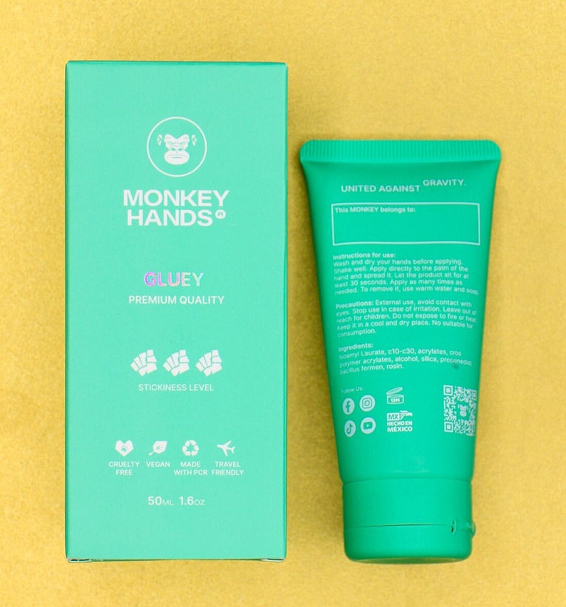 Pu&ograve; includere: Un tubo verde di crema per le mani con le parole "United Against Gravity" e "This Monkey belongs to..." sul davanti. Il retro del tubo elenca le istruzioni per l'uso, gli ingredienti e le icone dei social media. Il tubo &egrave; accanto a una scatola verde con le parole "Monkey Hands Gluey Premium Quality" e "Stickiness Level" sul davanti. La scatola ha anche icone per cruelty-free, vegano, realizzato con PCR e adatto ai viaggi. La scatola indica la dimensione come 50 ml o 1,6 oz.