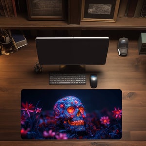 May include: A decorative mouse mat with a detailed skull design. The skull is blue with intricate patterns and glowing orange accents, set against a dark background with pink flowers. A keyboard, mouse, and monitor are visible.