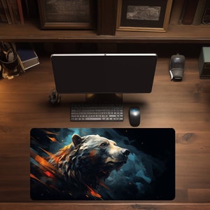 May include: A black and blue mousepad with a stylized illustration of a bear's head. The bear is facing right and has a dark brown fur with a white muzzle. The background is a dark blue with streaks of orange and yellow.