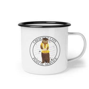 May include: White enamel mug with a black rim and handle. The mug features a circular design with the text "Crescent City Postal Service" and an illustration of an otter wearing a yellow vest.