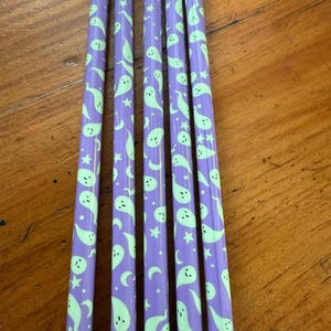 May include: Six purple pencils with a repeating pattern of green ghosts and stars. The pencils are all the same length and have a rounded tip.