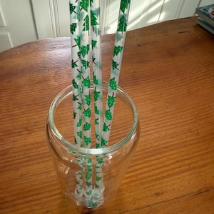 May include: Five clear plastic drinking straws with a green and white Christmas tree pattern. The straws are in a clear glass jar.