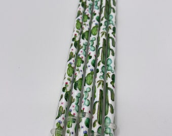May include: A set of six reusable drinking straws with a cactus and flower pattern. The straws are white with green and pink accents.