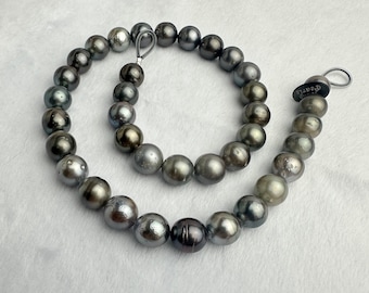 May include: A necklace of iridescent, dark gray pearls. The pearls vary in color, with hints of silver, black, and green. The necklace is strung on a silver chain and has a clasp. The word "Pearls" is printed on a small tag.