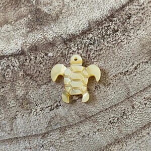 May include: A small, golden, shell turtle charm. The turtle is made of a smooth, shiny material and has a detailed shell pattern.