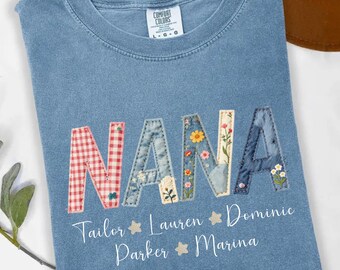 May include: A blue jean colored t-shirt featuring the word NANA in large, patterned, stitched-style letters. Below the word, the names Tailor, Lauren, Dominic, Parker, and Marina are printed in white script, separated by small star icons.