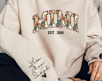 May include: A beige crewneck sweatshirt featuring the word MIMI in a floral pattern with the text EST. 2018 underneath. The right sleeve displays the names Lisa, Jhon, and Sarah written in black script above a small black heart icon.