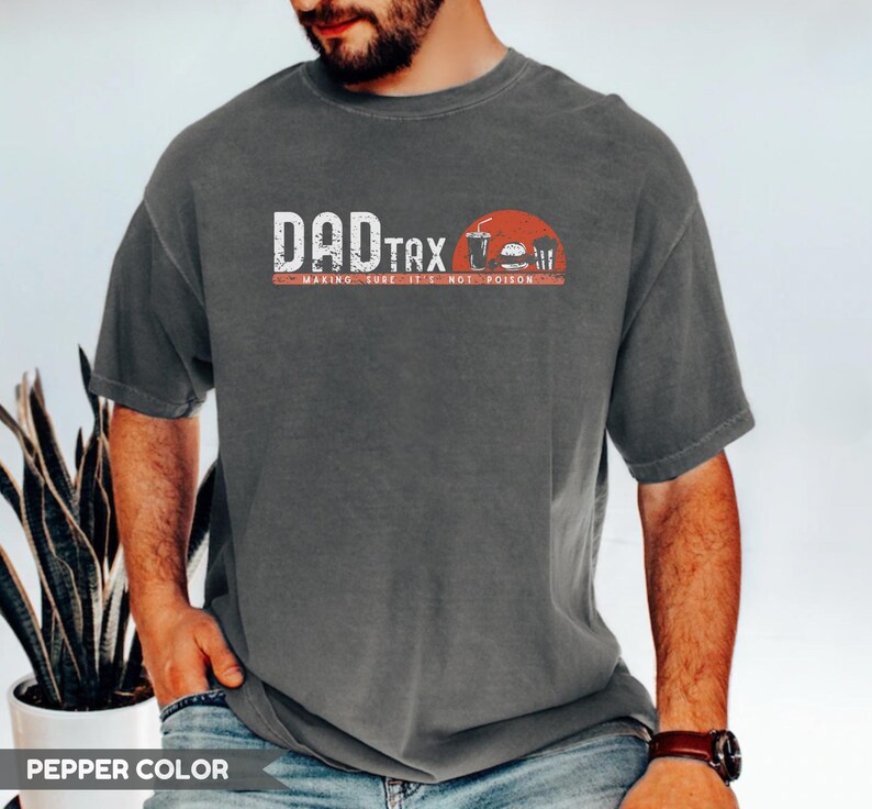 May include: Pepper color t-shirt with the text "DAD TAX" in white and red, along with a graphic of a burger, fries, and a drink. The text "MAKING SURE IT'S NOT POISON" is below the main text.