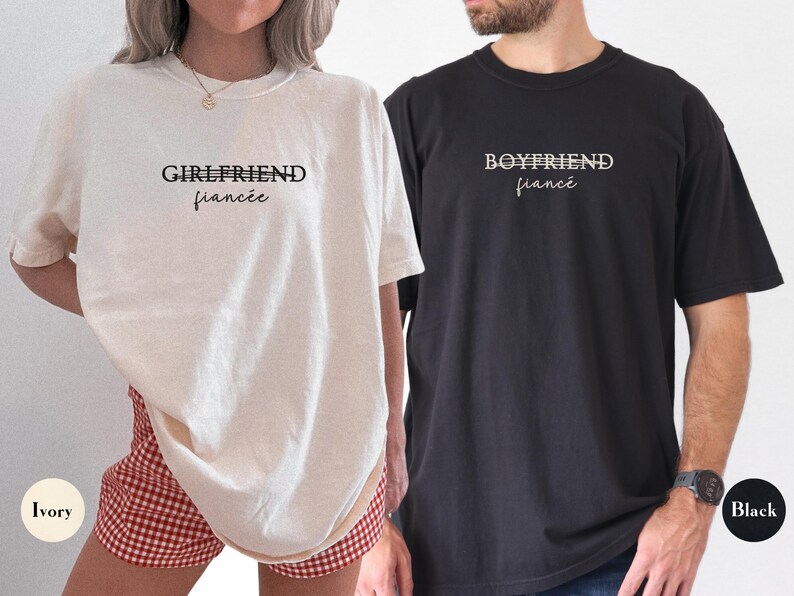 May include: Two t-shirts, one ivory and one black, with the words "GIRLFRIEND fianc&eacute;e" and "BOYFRIEND fianc&eacute;" printed on the front. The ivory shirt is paired with red and white checkered shorts. The black shirt is paired with blue jeans.