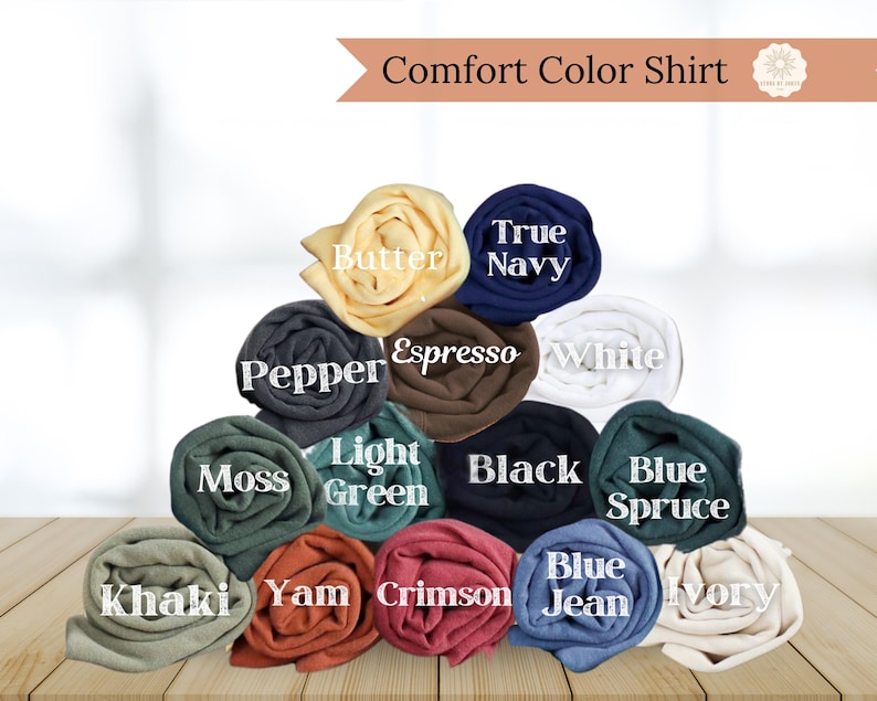 May include: A display of rolled Comfort Color shirts in various colors, including Butter, True Navy, Pepper, Espresso, White, Moss, Light Green, Black, Blue Spruce, Khaki, Yam, Crimson, Blue Jean, and Ivory. The text "Comfort Color Shirt" is at the top.