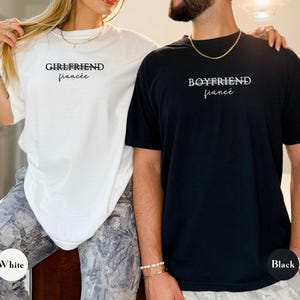 May include: White and black t-shirts with the words "Girlfriend fianc&eacute;e" and "Boyfriend fianc&eacute;" printed on them. The white shirt has a white circle with the word "White" on it. The black shirt has a black circle with the word "Black" on it.
