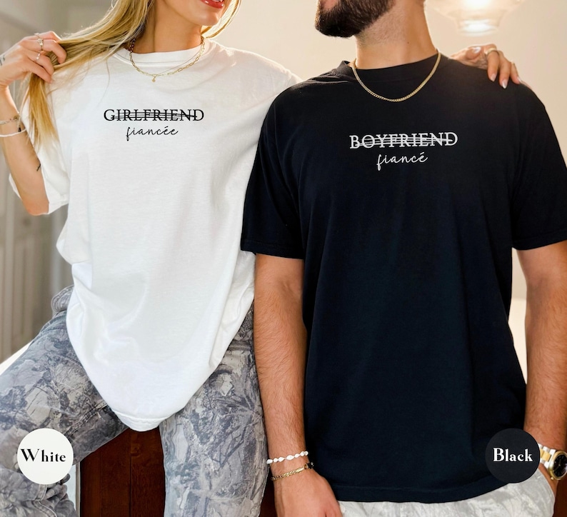 May include: White and black t-shirts with the words "Girlfriend fianc&eacute;e" and "Boyfriend fianc&eacute;" printed on them. The white shirt has a white circle with the word "White" on it. The black shirt has a black circle with the word "Black" on it.