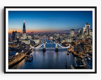 May include: A framed print of London at dusk, featuring the illuminated Tower Bridge and the Shard skyscraper. The cityscape is set against a gradient sky of blue and orange hues, with lights reflecting on the water.