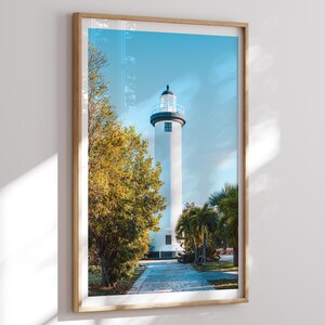 Pode incluir: Impressão emoldurada com um farol branco contra um céu azul claro. O farol tem um topo preto e uma varanda circular. Árvores verdes e palmeiras emolduram a estrutura, com um caminho pavimentado que leva a ela.