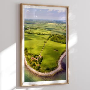 Puede incluir: Fotografía aérea de un paisaje verde con campos, árboles y una costa, enmarcada en un marco de madera marrón claro. La imagen muestra un día soleado con sombras, capturando la belleza natural del campo.