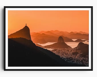 May include: A framed print of Rio de Janeiro at sunset. The image features the Christ the Redeemer statue atop a mountain, silhouetted against an orange sky. The city and surrounding mountains are visible in the background.