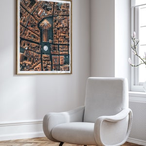 May include: An aerial photograph of a city with a large building in the center. The building has a dome and is surrounded by smaller buildings. The photo is framed in a wooden frame and hanging on a white wall.