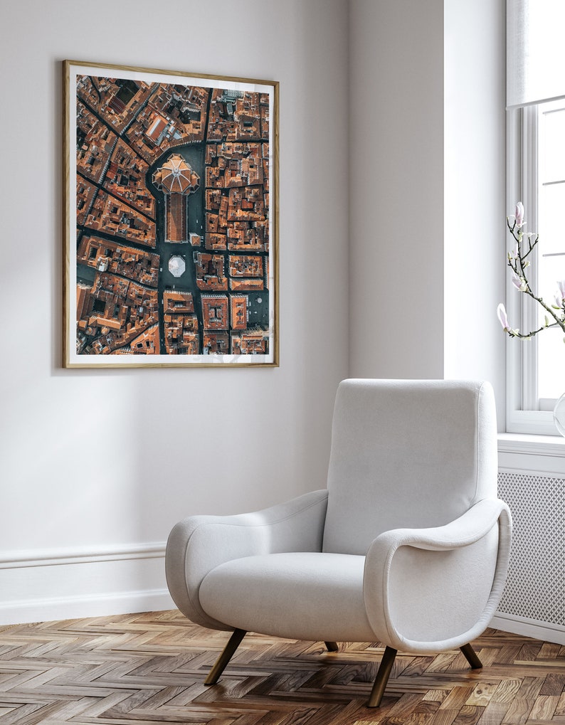 May include: An aerial photograph of a city with a large building in the center. The building has a dome and is surrounded by smaller buildings. The photo is framed in a wooden frame and hanging on a white wall.