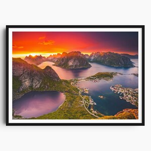 May include: A framed print of a coastal landscape at sunset. The sky is ablaze with orange and purple hues, casting light over the mountains and the sea. The image captures a serene view of the rugged coastline and the calm waters.