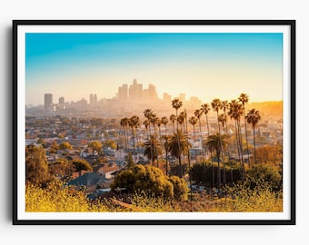 May include: A framed print featuring a cityscape with palm trees in the foreground and a skyline in the distance. The sky transitions from blue to yellow, suggesting sunrise or sunset. The image is framed in black.