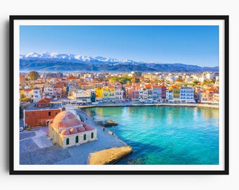 May include: A framed print depicting a picturesque coastal town with brightly coloured buildings bordering a turquoise harbour. Snow-covered mountains are in the background under a clear blue sky. A historic building with a red dome is in the foreground.