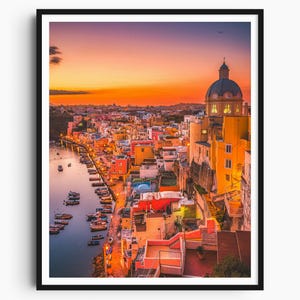 May include: A framed print of a coastal town at sunset. The image shows colorful buildings, a harbor with boats, and a church with a domed roof. The sky changes from orange to purple.
