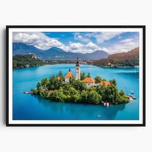 Può includere: Stampa incorniciata del lago di Bled in Slovenia, con una chiesa su una piccola isola al centro del lago. L'acqua è di un blu vibrante, con montagne e nuvole sullo sfondo. La stampa è in una cornice nera.