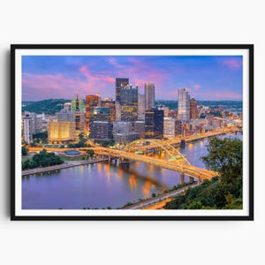 Peut inclure: Impression encadrée d'un paysage urbain au crépuscule. L'image présente une rivière, un pont avec des lumières jaunes et une ligne d'horizon de bâtiments illuminés. Le ciel passe du rose au bleu.