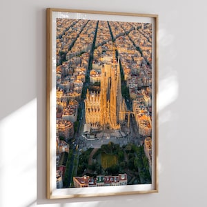 Könnte beinhalten: Luftaufnahme der Sagrada Familia in Barcelona, Spanien, gerahmt in hellem Holz. Das Bild zeigt die komplizierte Architektur der Basilika, eingebettet in die Stadtlandschaft, die von warmem Sonnenlicht durchflutet wird.