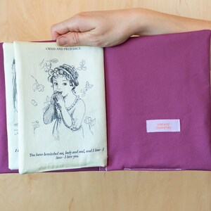 May include: A purple book sleeve holds a vintage book page with a black and white illustration and text from "Pride and Prejudice." The sleeve has a small rectangular label with text. The book is open, revealing the printed pages.